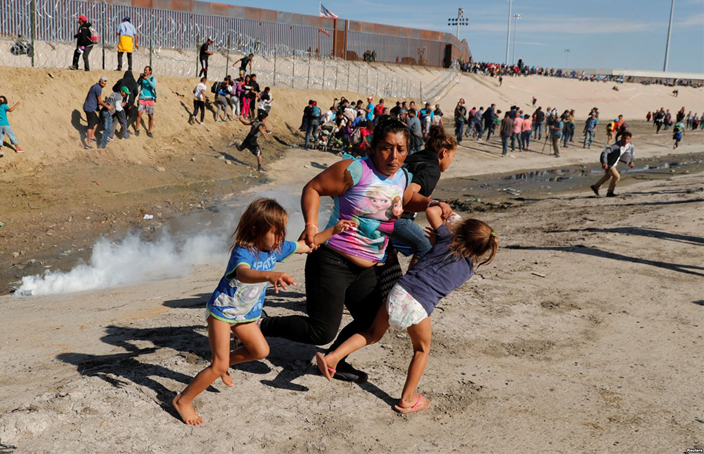 Una familia de migrantes, parte de la caravana de miles que viaja desde Centroamérica hacia Estados Unidos, corre para escapar del gas lacrimógeno en la frontera entre Estados Unidos y México en Tijuana, el 25 de noviembre del 2018. Foto: Voz de América