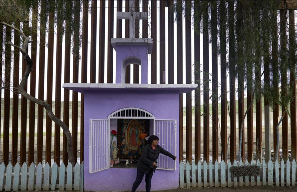 En esta foto de enero 16 de 2019, Esther Arias abre una ventana en una capilla construida por su padre José Arias delante de una renovada sección de una valla fronteriza de acero en Tijuana, México. | Foto: Voz de América