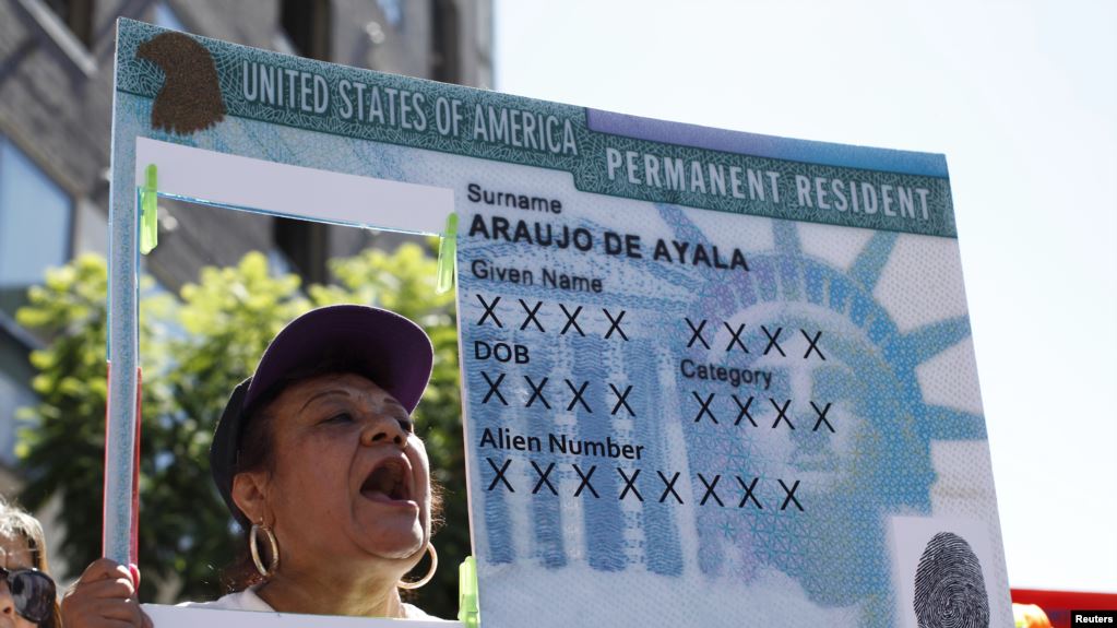 Imagen de archivo de una mujer levantando un cartel con una réplica de tarjeta de residencia. | Foto: Voz de América / Reuters/Lucy Nicholson