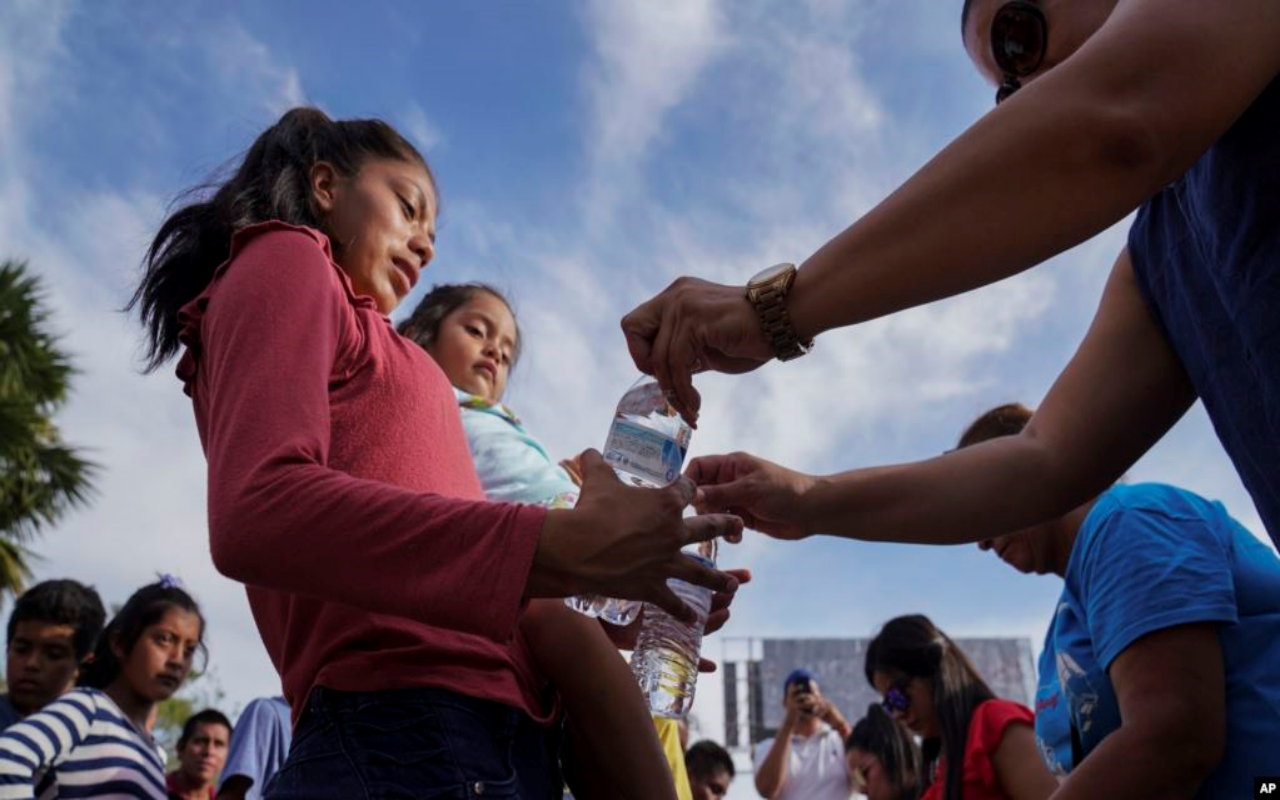 Voluntarios entregan botellas de agua a decenas de migrantes, muchos de los cuales fueron devueltos a México bajo el programa "Permanecer en México" del gobierno de Donald Trump, en un campamento en Matamoros, México.