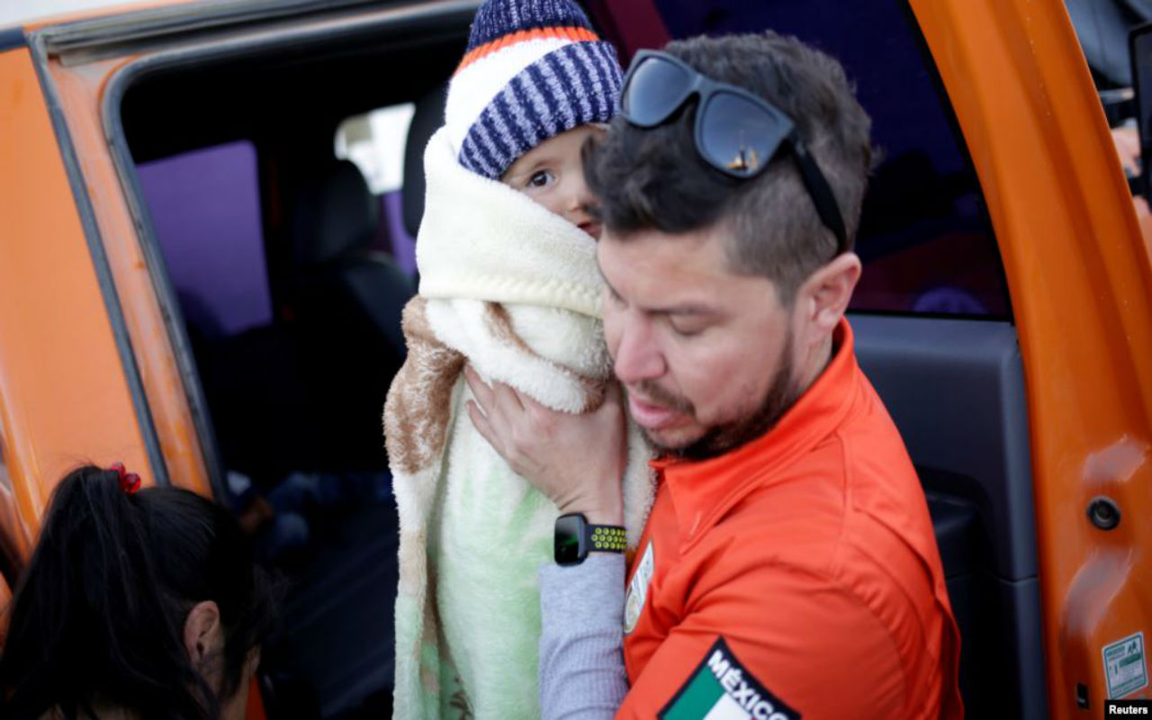 Un funcionario del gobierno de Ciudad Juárez sostiene al hijo de un peticionario de asilo mexicano, que con su familia acampaban cerca del cruce fronterizo de Paso del Norte, mientras esperaban para solicitar asilo en EEUU, porque se les mudará a un refugio local. Reuters.