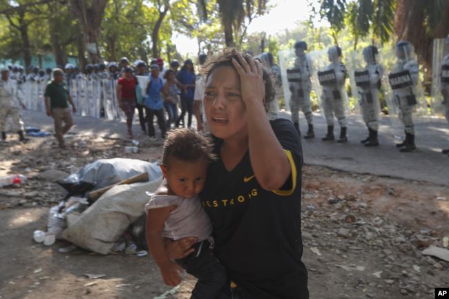 Una mujer migrante con un niño se aleja de la Guardia Nacional Mexicana que bloquea el paso a un grupo de migrantes centroamericanos cerca de Tapachula, México, el jueves 23 de enero de 2020.