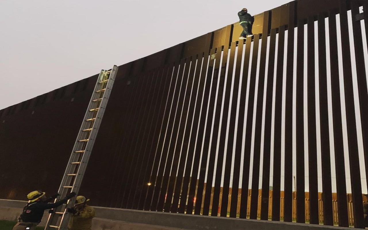 Migrante mexicano atrapado en lo alto del muro fronterizo