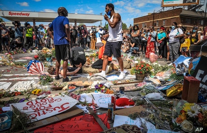 El organizador de la comunidad Tommy McBrayer, a la derecha, usa un megáfono mientras dirige una recreación del encuentro de George Floyd con la policía.