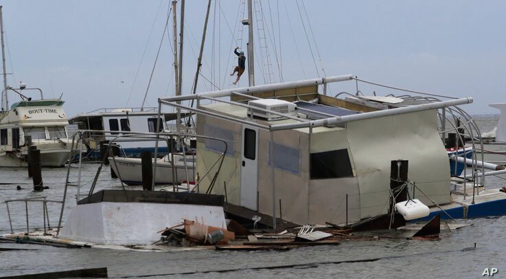 Matthew Howard sube al mástil de su barco mientras examina el daño a un puerto deportivo privado después de que fue golpeado por el huracán Hanna, el domingo 26 de julio de 2020, en Corpus Christi, Texas. Foto: VOA, AP