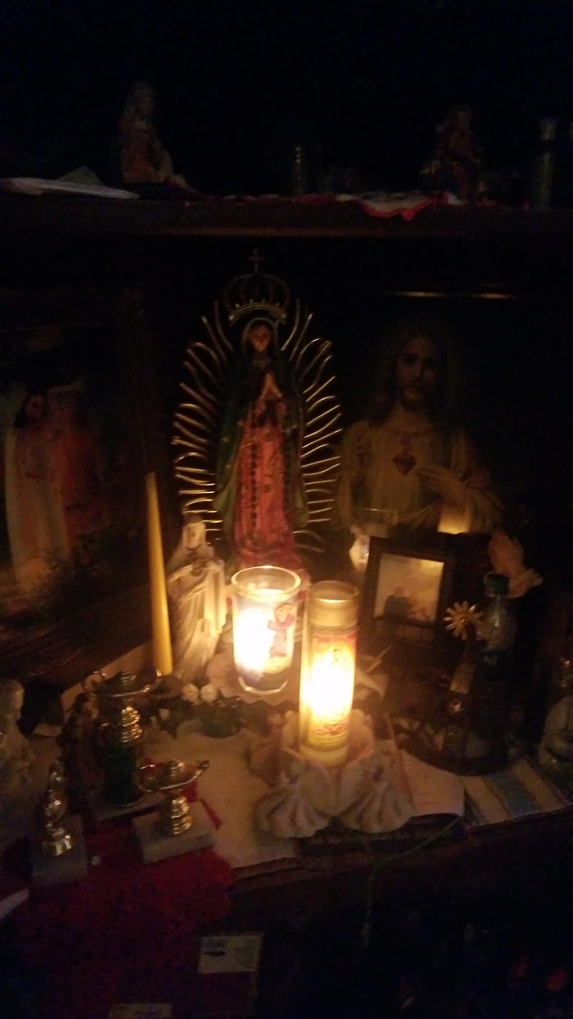 Altar con la Virgen de Guadalupe y el Sagrado Corazón de Jesús con veladoras y fotografías 
