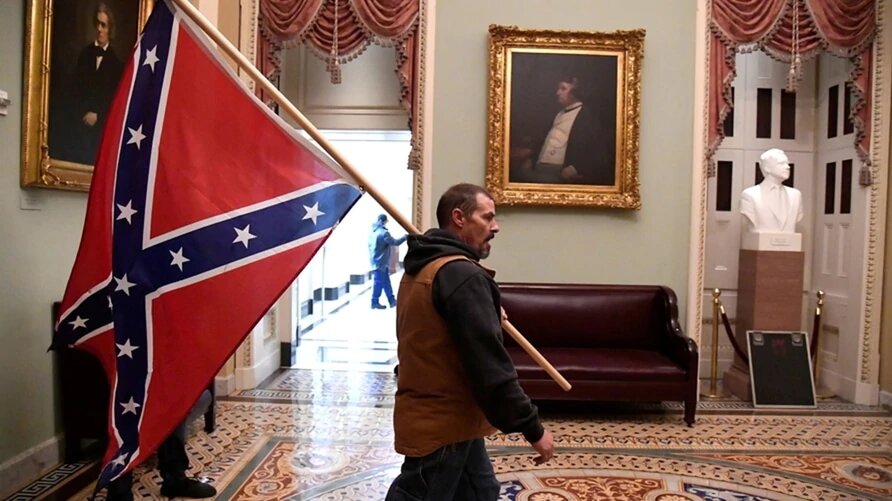 Un simpatizante de Donald Trump porta una bandera confederada en el segundo piso del Capitolio, luego de irrumpir con violencia al edificio, el 6 de enero de 2021. | Foto: Voz de América.
