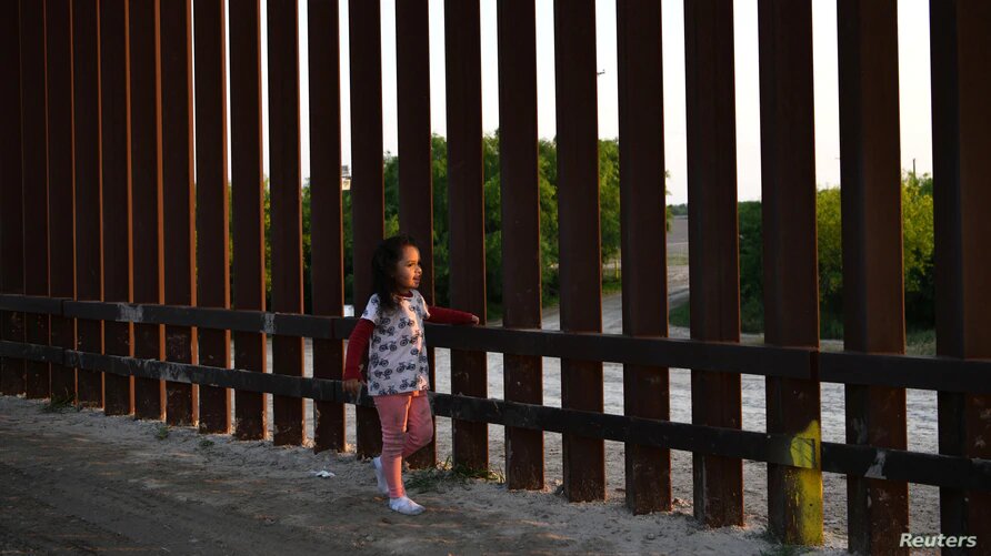 Dos bases militares en Texas resguardarán a niños migrantes no acompañados. Una pequeña, que forma parte de un grupo de migrantes llegados de Centroamérica, camina junto a la valla fronteriza que separa Estados Unidos y México, tras entrar al país de manera irregular, el 6 de abril de 2019. | Foto: Reuters / VOA.