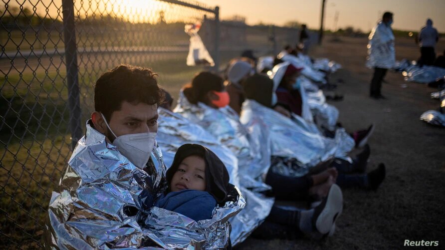 Migrantes centroamericanos con niños esperan en un campo de béisbol después de cruzar el Río Grande hacia Estados Unidos en balsas. La Joya, Texas, 19 de marzo de 2021. | Foto: Reuters / VOA.