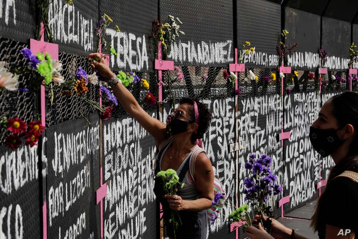 Mujeres colocan flores en una cerca perimetral instalada frente al Palacio Nacional horas antes de la manifestación por el Día Internacional de la Mujer, en la Ciudad de México, el domingo 7 de marzo de 2021. | Foto: Reuters / VOA.