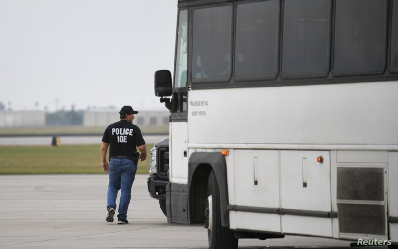 Un oficial de inmigración de EE. UU. camina al lado de un bus para transportar inmigrantes que serán deportados desde el aeropuerto internacional de Brownsville, Texas, en mayo de 2018. | Foto: Reuters / Voz de América