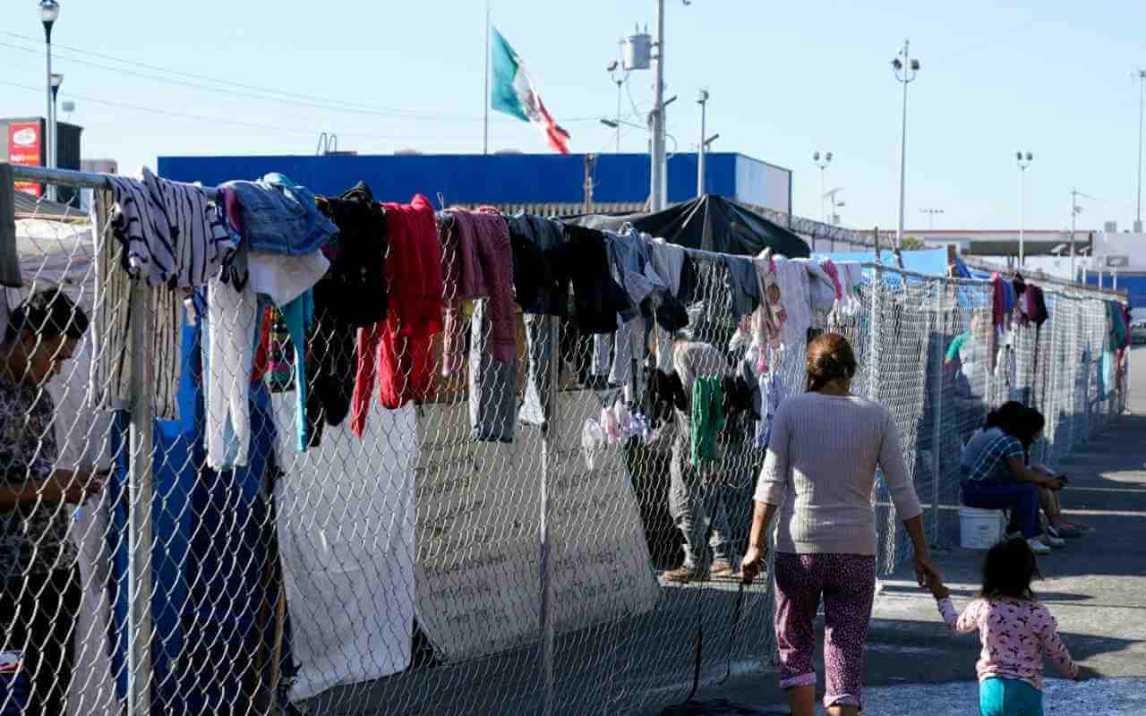 Migrantes caminan junto a la cerca de un campamento improvisado que bloquea la entrada a un cruce peatonal a Estados Unidos el 8 de noviembre de 2021, en Tijuana, México. | Foto: AP / Voz e América