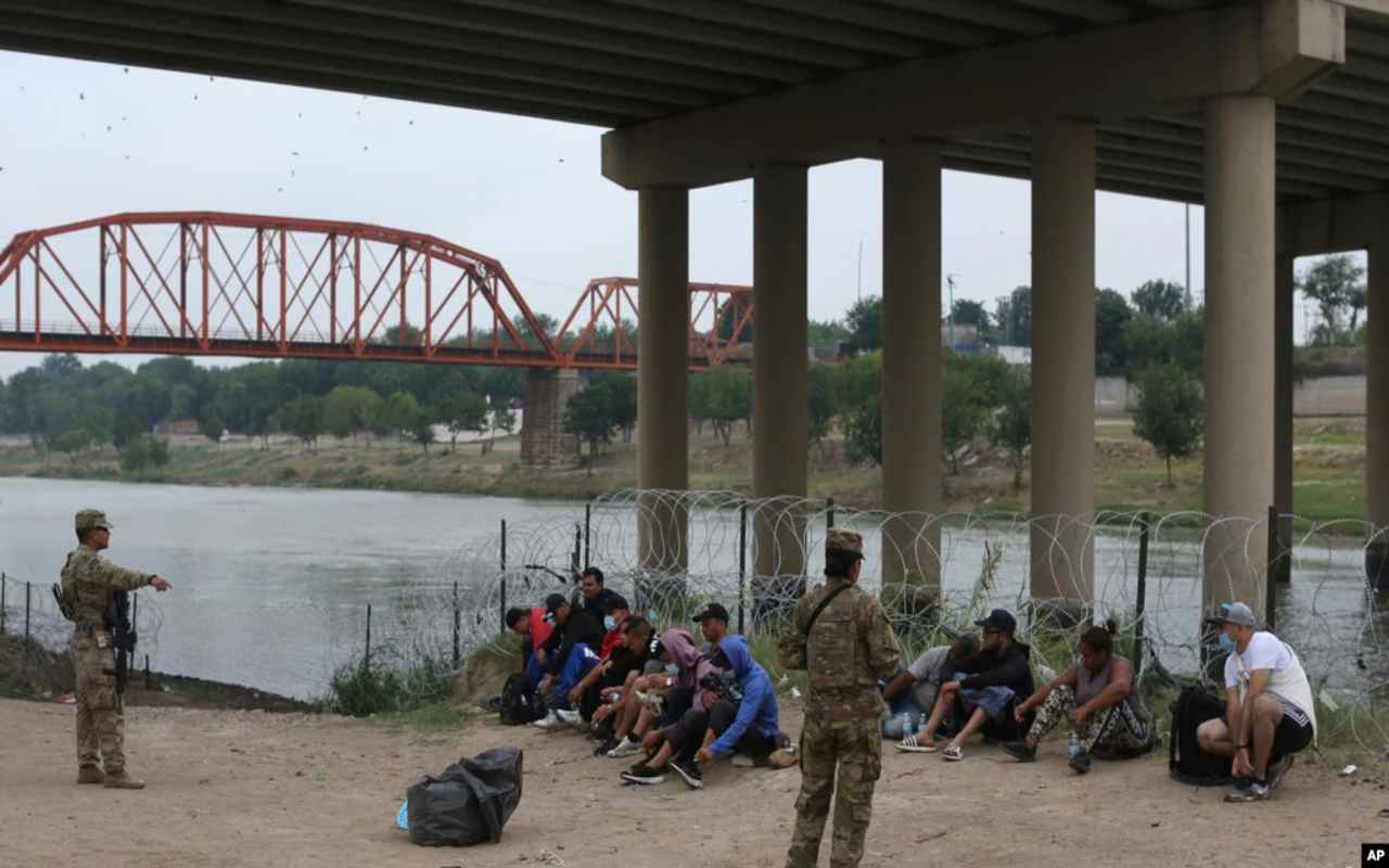 Los migrantes que cruzaron el río Bravo hacia EEUU están bajo la custodia de miembros de la Guardia Nacional mientras esperan la llegada de los agentes de la Patrulla Fronteriza para que los deporten a México bajo el Título 42. | Foto: VOA / AP.