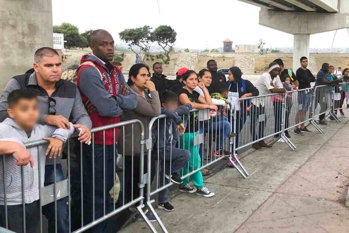 Solicitantes de asilo bajo Quédate en México escuchan si sus nombres son llamados en un cruce fronterizo con EEUU el 26 de septiembre de 2019. | Foto: AP / Voz de América